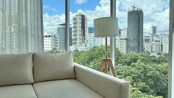 Un salón moderno con un ventanal grande, un sofá, una lámpara y vistas a la ciudad.
