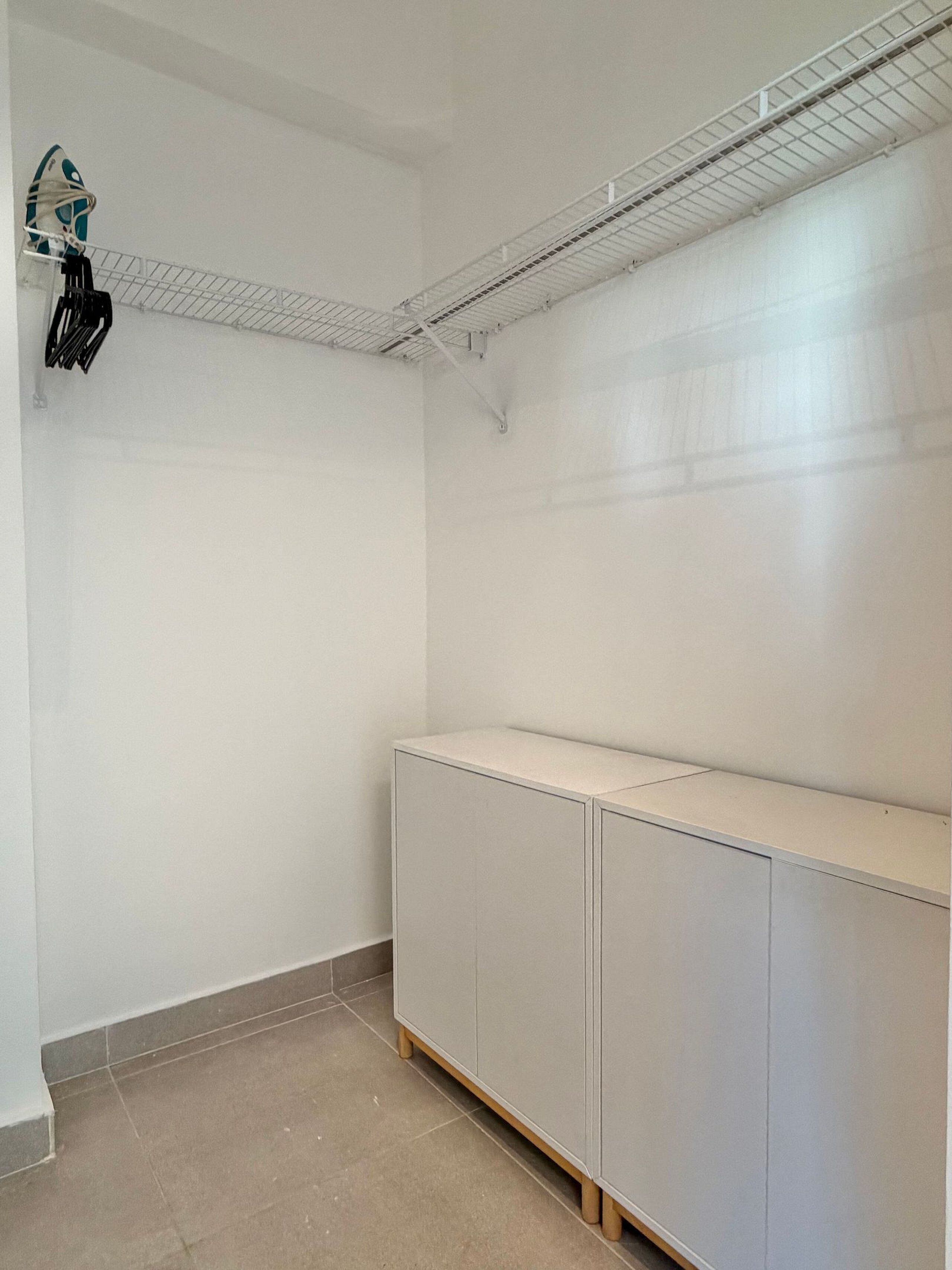 Una habitación con un armario blanco, una estantería de metal y suelo de baldosas.