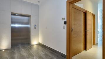 A hallway with a metallic elevator and wooden doors, a number sign 'B7', and a tiled floor.