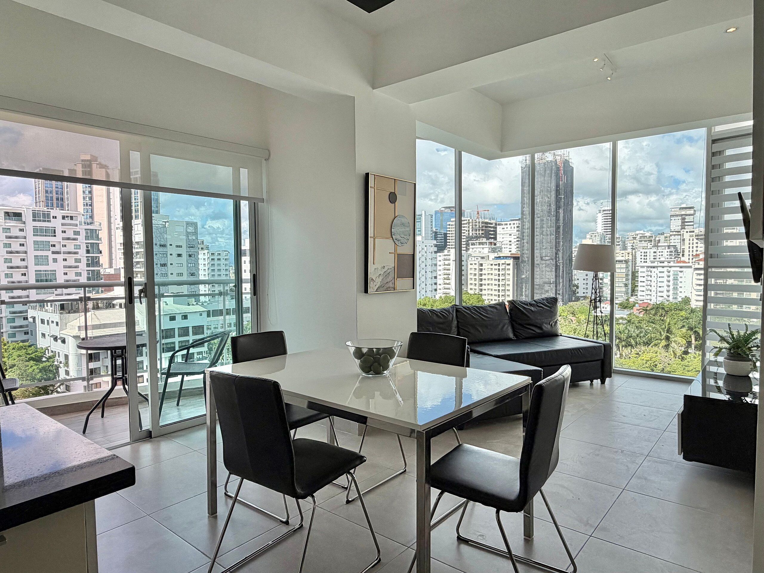 A modern living room with a dining area, large windows offering city views, and a minimalist design.