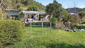 Una casa con porche cubierto, patio cercado y montañas al fondo.