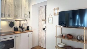 A compact kitchen with white cabinets, a wooden countertop, and a built-in oven. A large flat-screen TV is mounted on the wall above a wooden shelf with dishes. - Design Studio in Navigli | Wi-Fi & Self Check-in (Milano)
