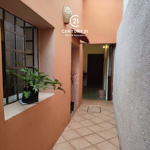 A narrow corridor with a tiled floor, a window with a potted plant, and a door leading to another room. - La Casita de Regina, Beautiful typical Centro house, your Home. (Oaxaca de Juárez)