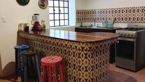 Een keuken met een centraal eiland, een fornuis en een spoelbak. Er staan twee krukken bij en aan de muur hangt een decoratief bord.