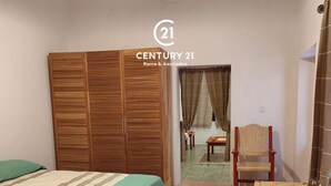 Een slaapkamer met een bed, een houten garderobe, een rieten stoel en een klein tafeltje.