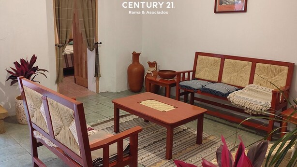 Een woonkamer met een bank, fauteuil en salontafel. Er is een deur naar een andere kamer, een vaas en een schilderij aan de muur.