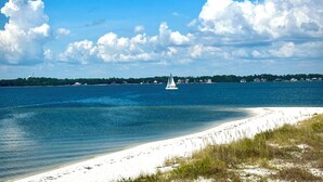 Ein Strand mit einem Segelboot auf dem Wasser, einem sandigen Ufer und einer fernen Küstenlinie mit Gebäuden.