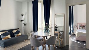 A modern living room with a sofa, dining table, and chairs. There is a mirror on the wall, a lamp, and a window with curtains. - ACasaDiImma | Penthouse with Terrace | Wi-Fi (Milano)