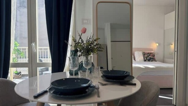 A dining area with a round table, chairs, a vase with flowers, and a mirror on the wall. - ACasaDiImma | Penthouse with Terrace | Wi-Fi (Milano)