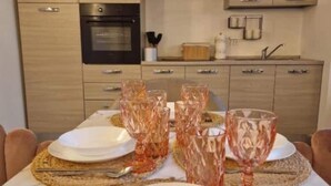 Una mesa de comedor dispuesta con platos, vasos y cubiertos, con una cocina al fondo.