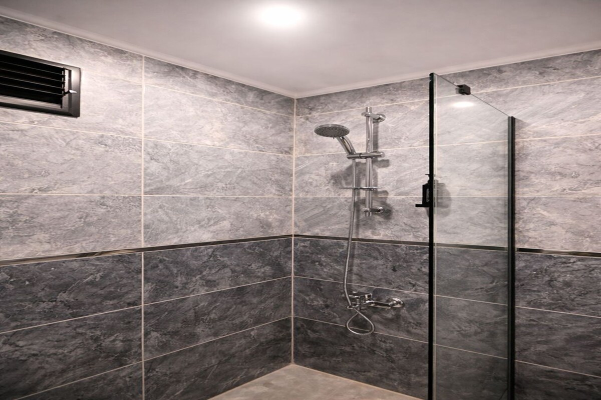 Eine moderne Dusche mit Glastür, Duschkopf zum Anfassen und einer fest montierten Bedienkonsole.