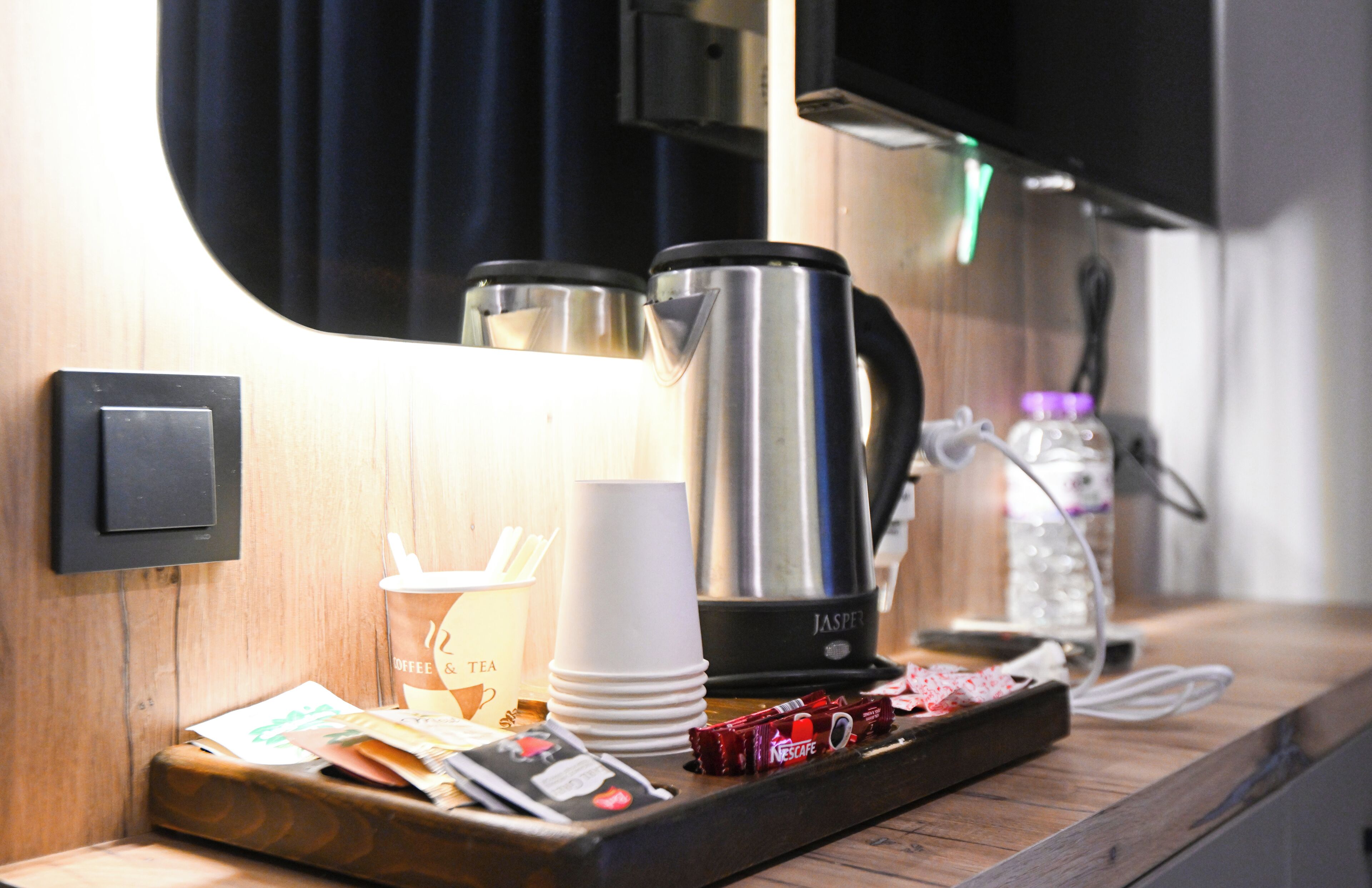 A coffee station with a coffee maker, cups, and a tray with coffee cups and a water bottle.