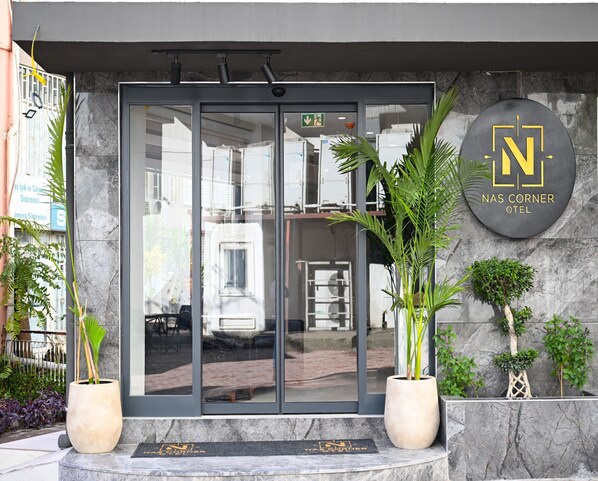 A hotel entrance with a glass door, potted plants, and a sign reading "Nasas Corner Hotel". - Nas Corner Hotel (Antalya)