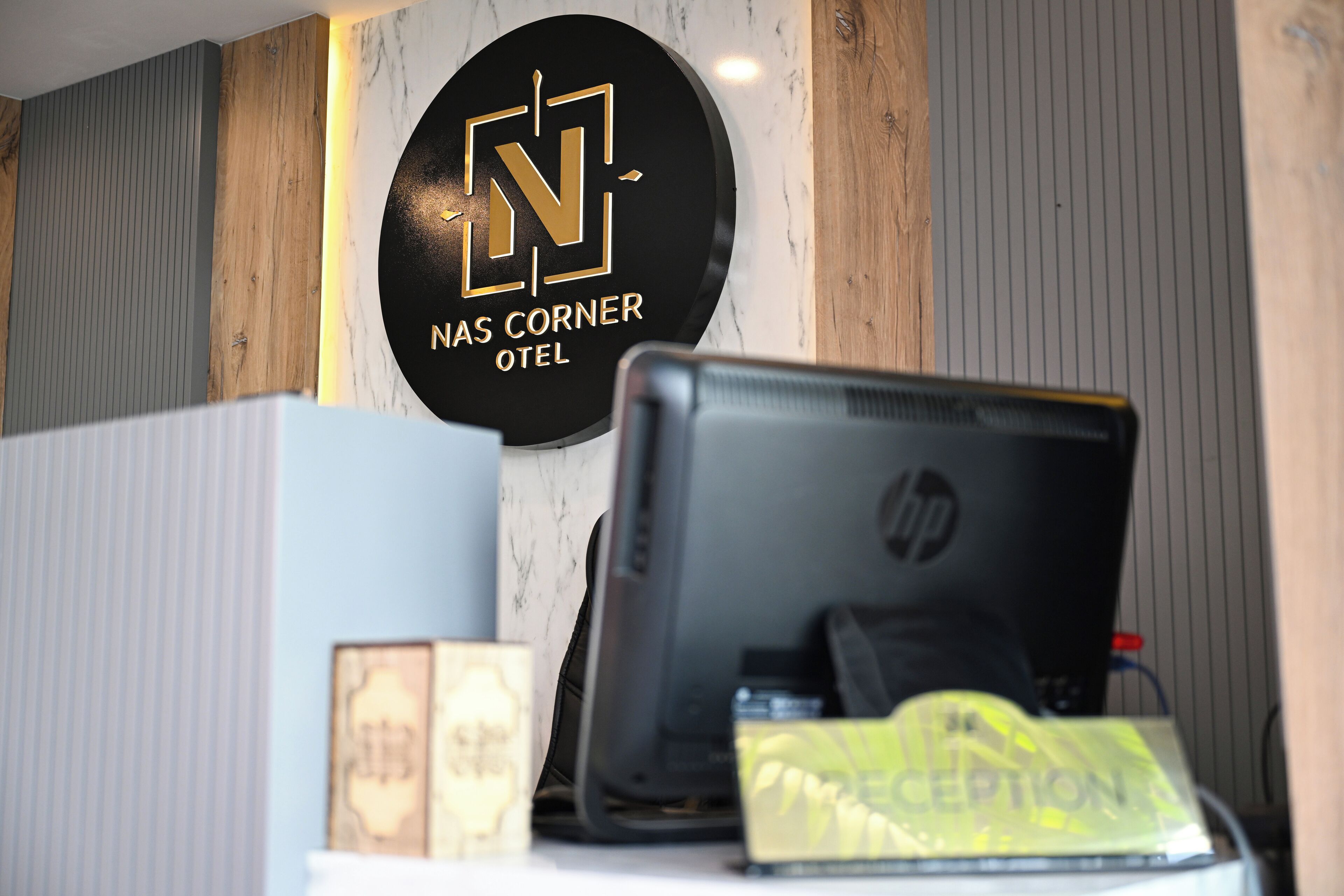 A reception desk with a computer, a reception bag, and a sign that reads "NAs Corner Hotel".
