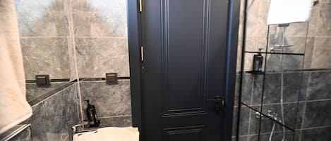 A bathroom with a white sink, dark tiled walls, a black door, and a shower area.