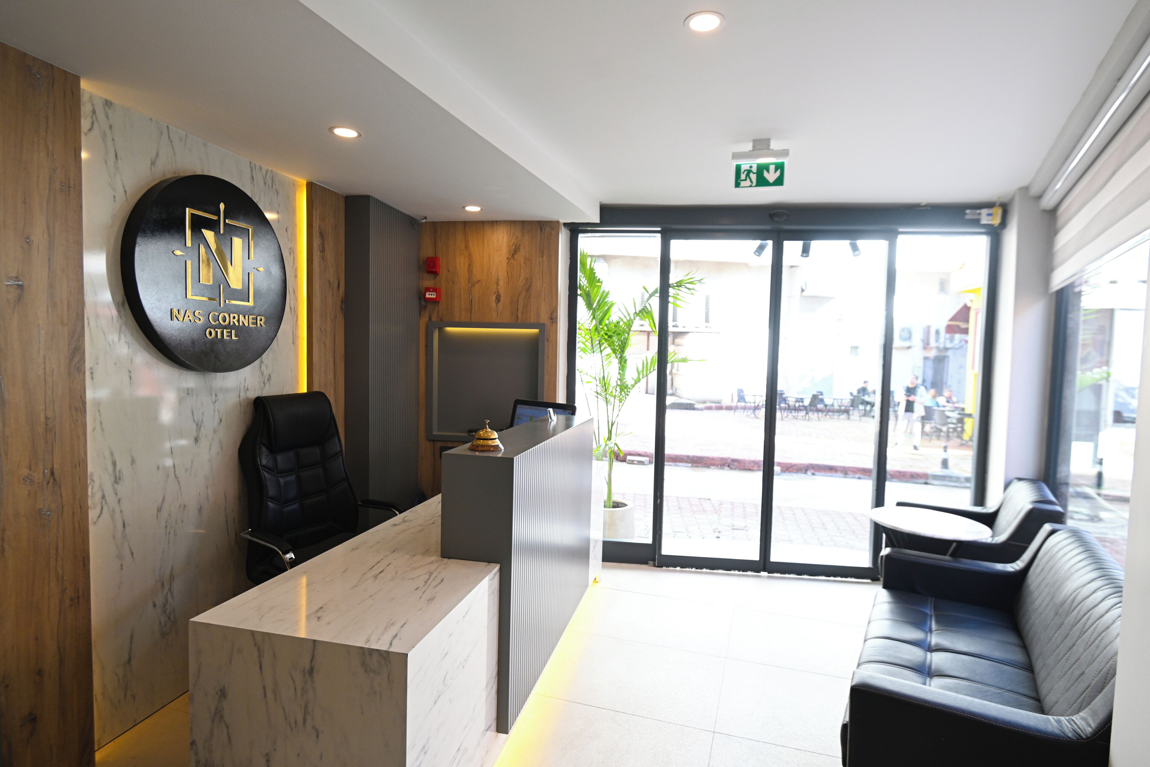 A hotel reception area with a marble reception desk, a black leather chair, a sofa, and a large window offering a view of the street.