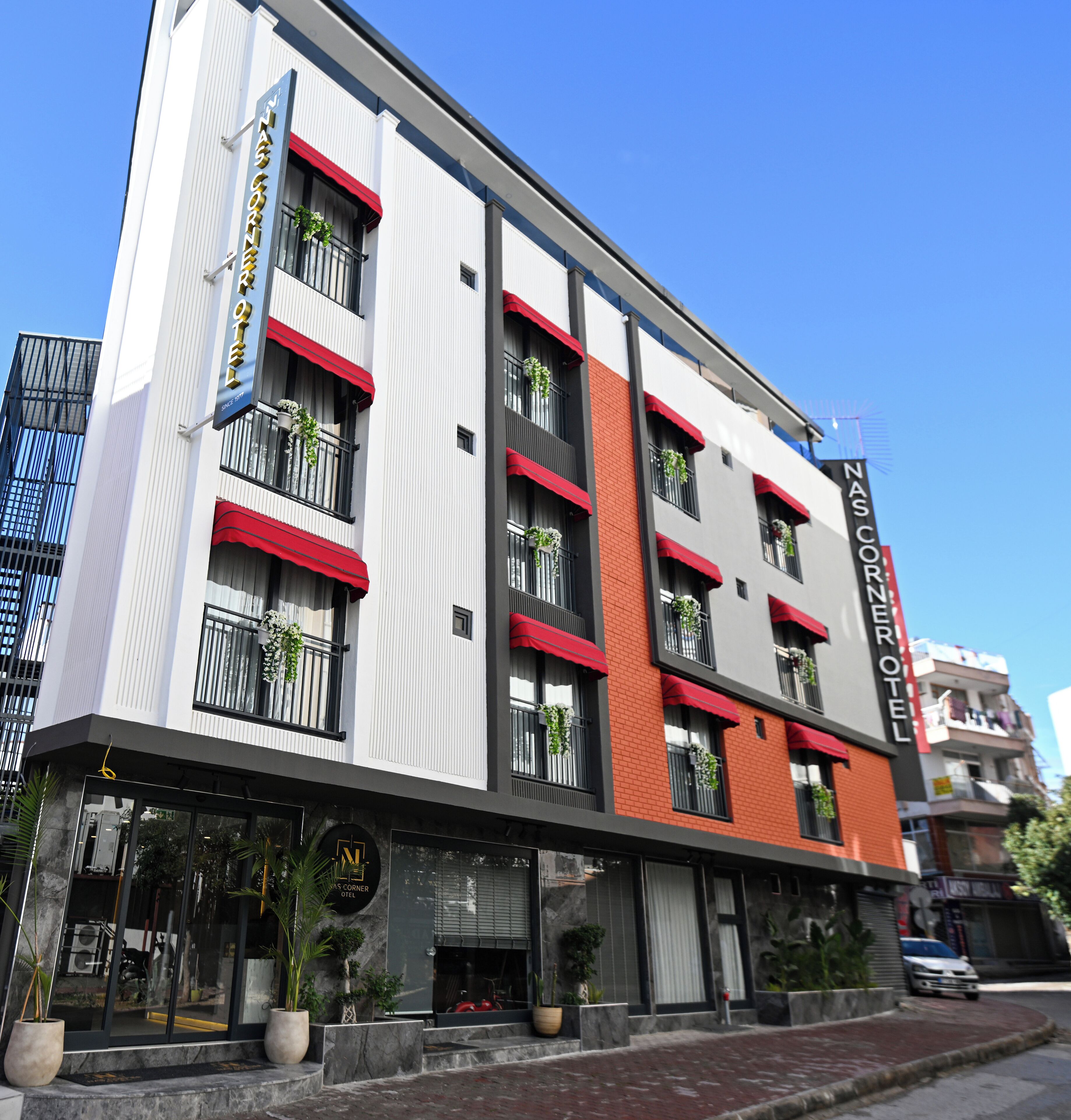 Un hotel modern amb diverses plantes, balcons amb plantes i un cel blau clar.