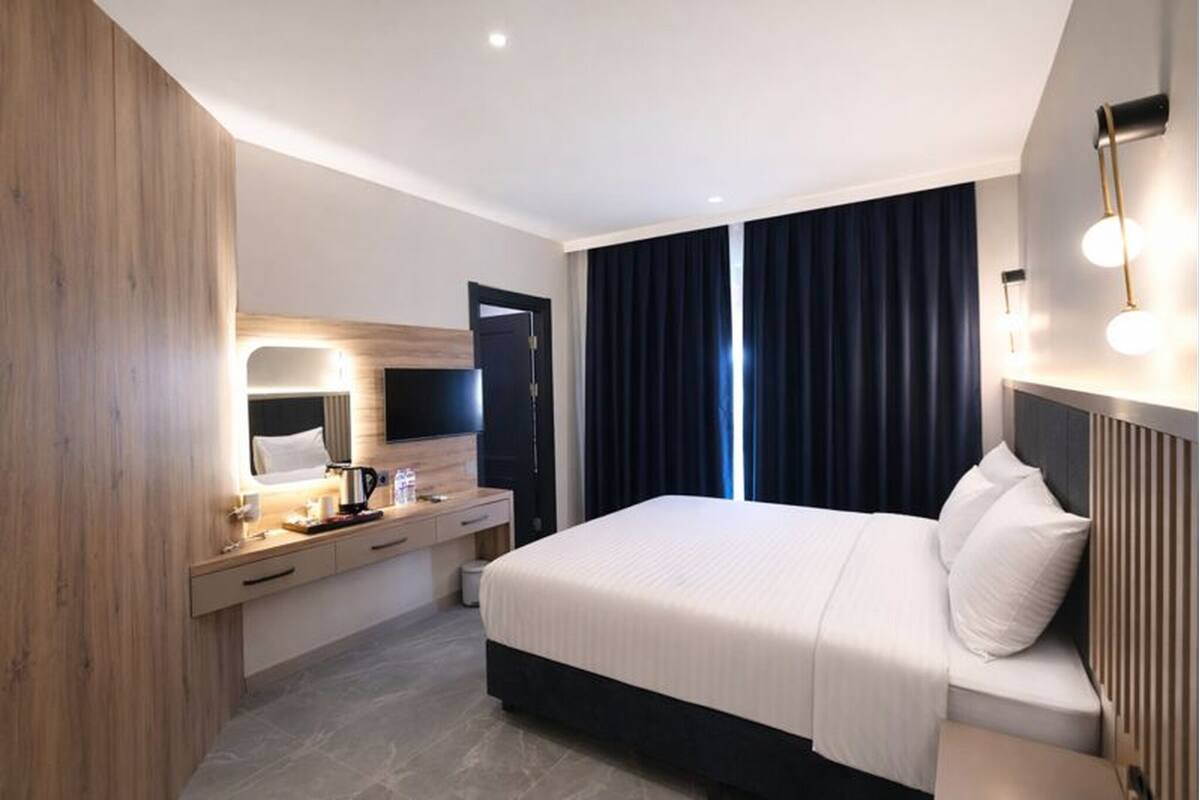 Una habitación de hotel moderna con cama, mesita de noche, espejo y televisor.