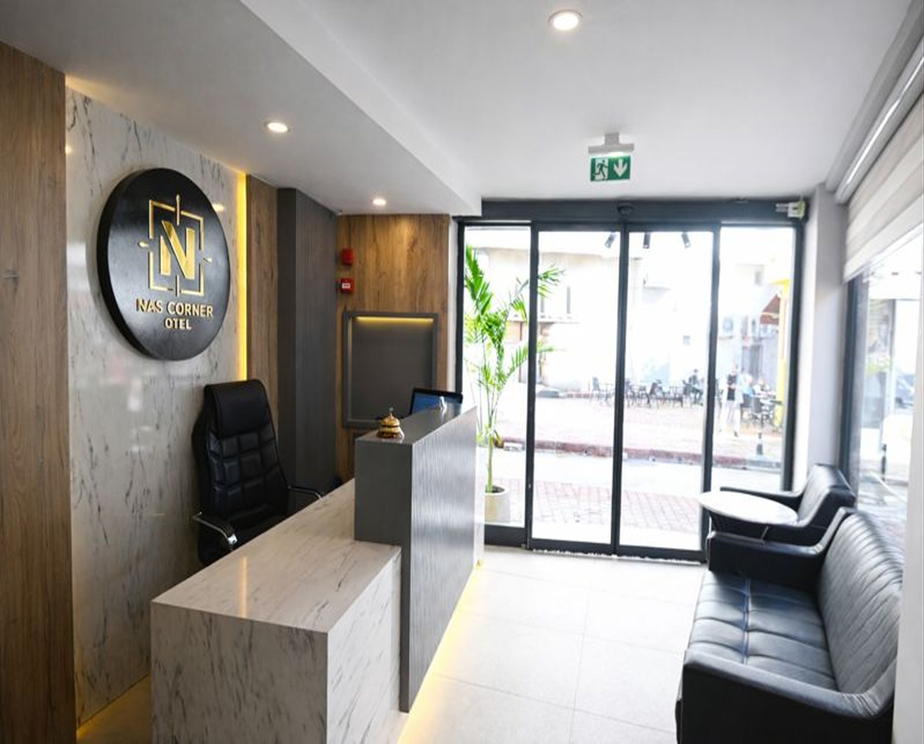 A hotel reception area with a marble reception desk, a black office chair, a sofa, and a large window with a view of the street.
