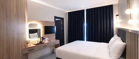 A modern hotel room with a large bed, a bedside table with a lamp, a flat-screen TV, and a window with dark curtains.