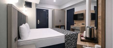 A modern hotel room with a bed, a desk, a mirror, and a coffee maker.