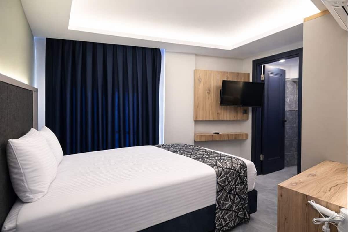 Habitación de hotel con cama, escritorio, televisor montado en la pared y puerta que da a otra habitación.