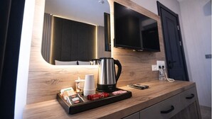 A modern hotel room with a wooden vanity, a flat-screen TV mounted above it, a coffee maker, and a tray with coffee cups and snacks. - Nas Corner Hotel (Antalya)