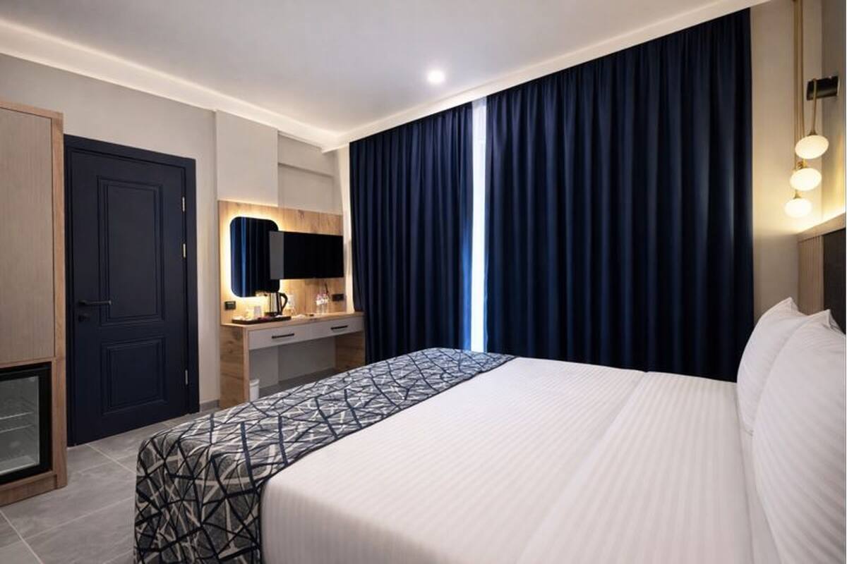 Una habitación de hotel con una cama grande, un escritorio con espejo, un armario y una ventana con cortinas.