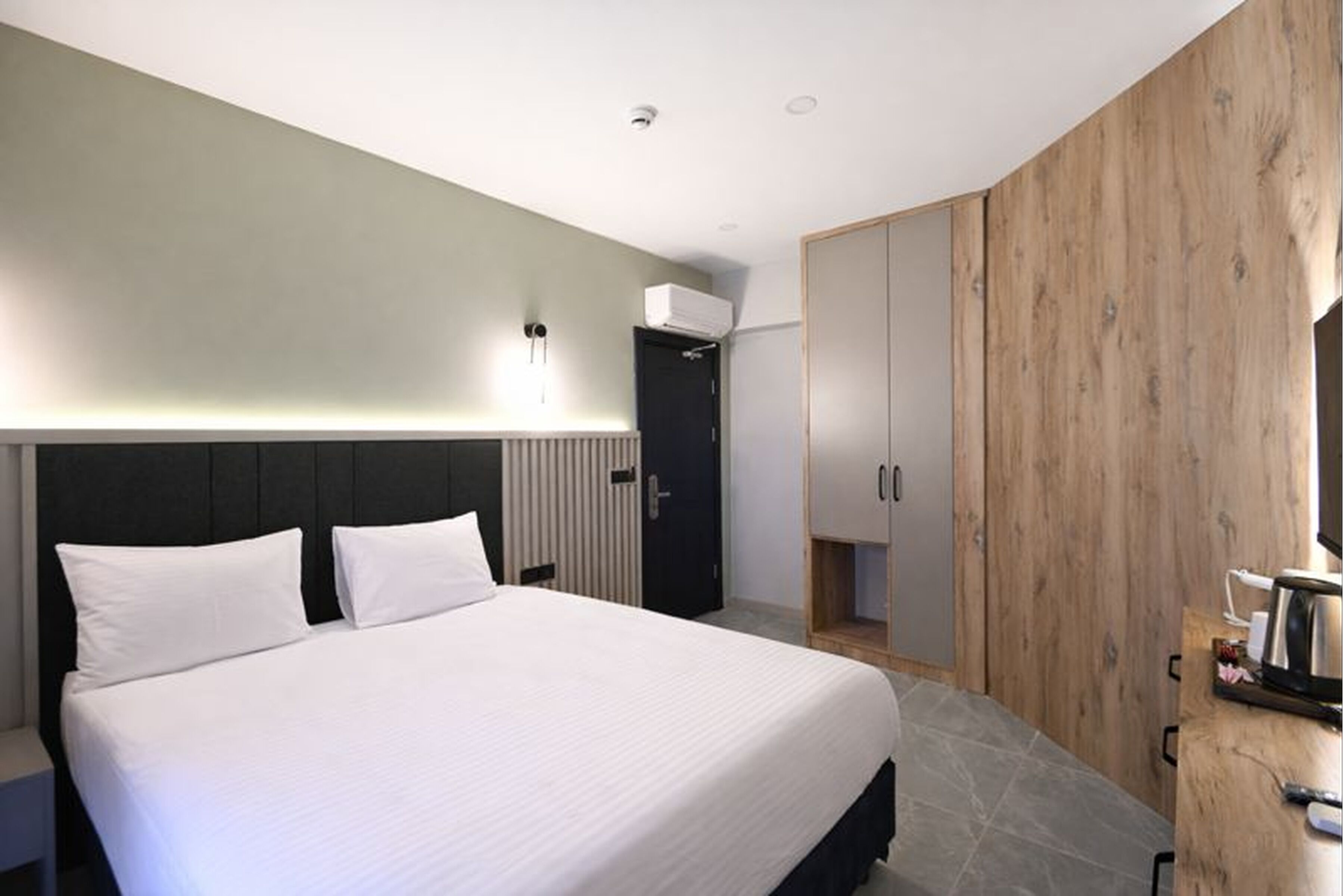 A modern hotel room with a large bed, a wooden wardrobe, and a built-in heater.