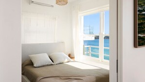 A bedroom with a large window offering a view of the sea and a boat. - Bondi Waterfront Pad (North Bondi)