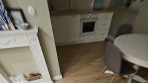 Une pièce avec un plancher en bois, une armoire blanche où sont rangées des chaussures, une table à manger grise et une chaise grise.