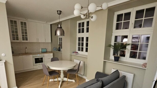 Une cuisine moderne avec des meubles blancs, une table à manger avec des chaises et un canapé gris.