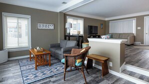 A living room with a grey sofa, a wicker chair, a small table, and a television. - Serene Waterfront Getaway | Patio and Dock (Marysville)