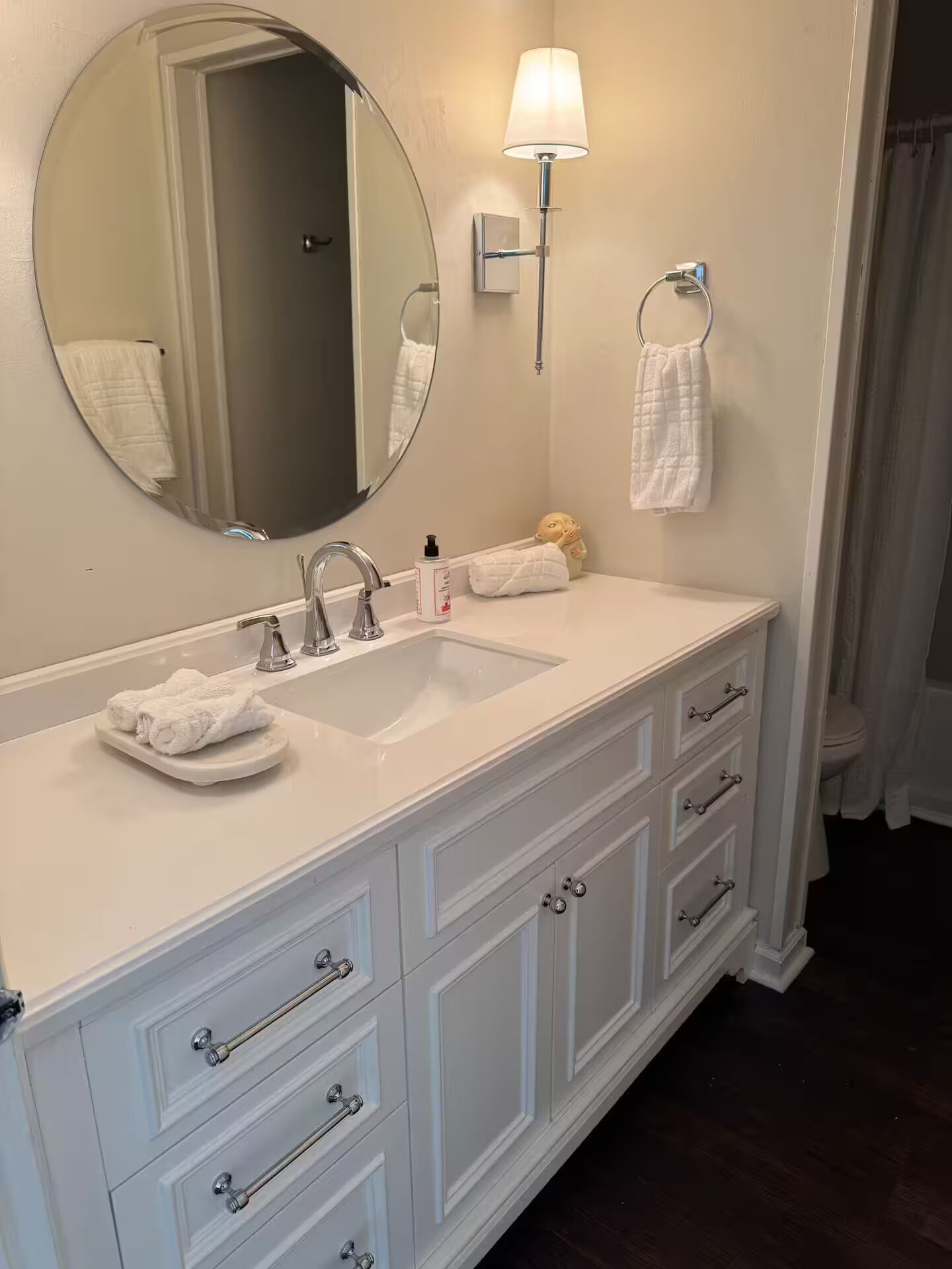 A bathroom with a white vanity, a round mirror, a sink, and a towel rack.