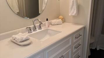 A bathroom with a white vanity, a round mirror, a sink, and a towel rack.