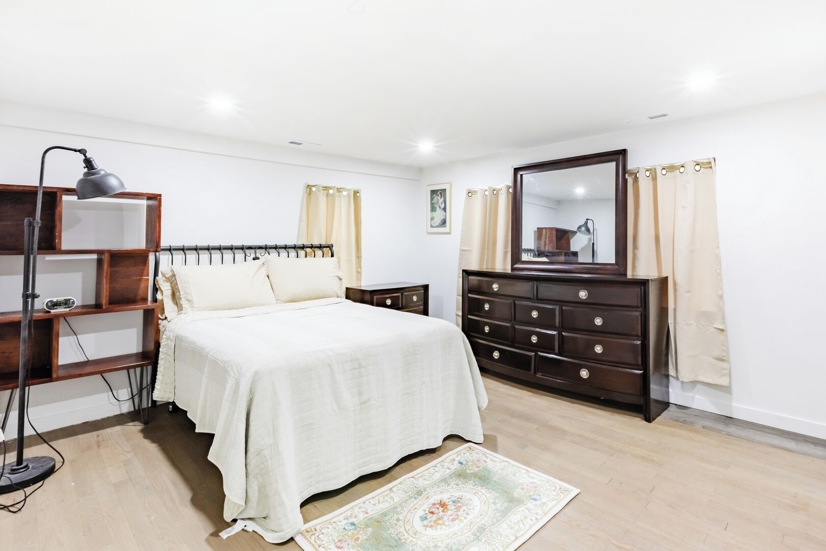 A bedroom with a bed, a dresser, a nightstand, a lamp, and a bookshelf.