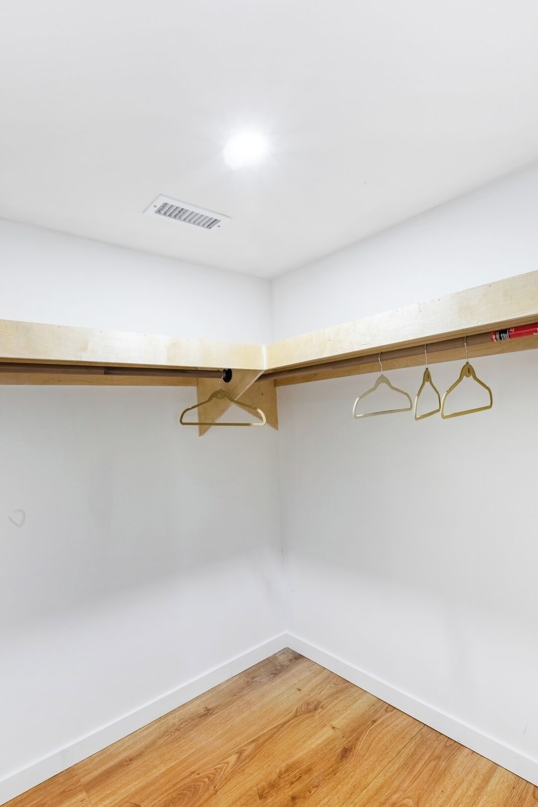 A corner room with white walls, wooden flooring, and a ceiling vent.