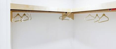 A corner of a room with white walls, a wooden floor, and two metal clothes hangers hanging from a wooden beam.