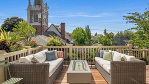 Eine Terrasse mit Korbmöbeln und einem Tisch mit Glasplatte, mit Blick auf eine Kirche und Wohnhäuser.