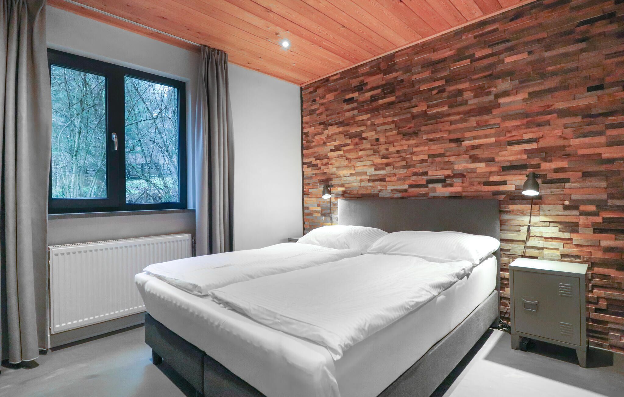 Un dormitorio moderno con cabecera de madera, una cama grande con ropa de cama blanca, una ventana con cortinas y un radiador.