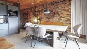 Una cucina moderna con soffitto in legno, parete a parete in pietra e zona pranzo con tavolo e sedie.