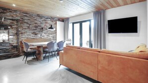 Un soggiorno moderno con soffitto in legno, una TV a parete, un divano e una zona pranzo con sedie e tavolo.