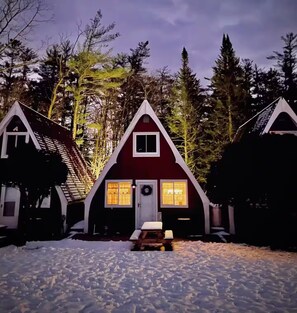 A cabin with a triangular roof, a front porch, and a snow-covered ground. - Gnome Home (Campton)