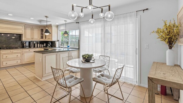 Een moderne keuken met een centraal eiland, hangende lampen en een eethoek met een ronde tafel en stoelen.