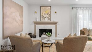 Een woonkamer met een open haard, twee fauteuils, een ronde salontafel en een groot abstract schilderij aan de muur.