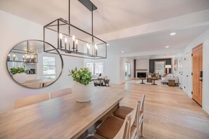 A spacious living area with a wooden dining table, a large mirror, and a modern chandelier. - @ Marbella Lane - Cozy Modern Home w/ Relaxing Design & Pool (Fullerton)