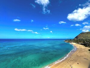 Ein Strand mit klarem türkisblauem Wasser, einem sandigen Ufer und einer hügeligen Kulisse.