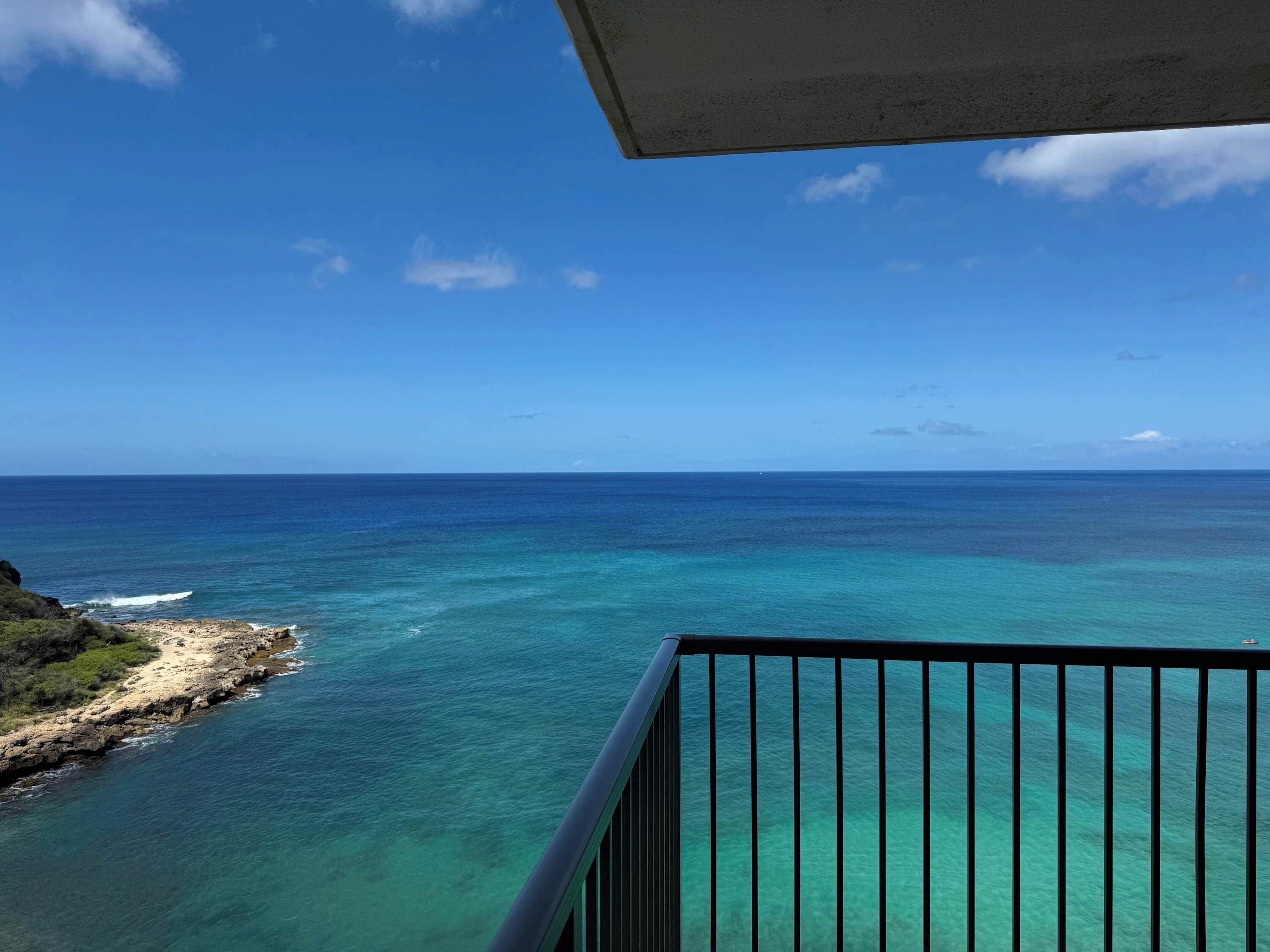 Ein Balkon mit Blick auf eine Küstenlandschaft, darunter ein Sandstrand und türkisfarbenes Wasser.