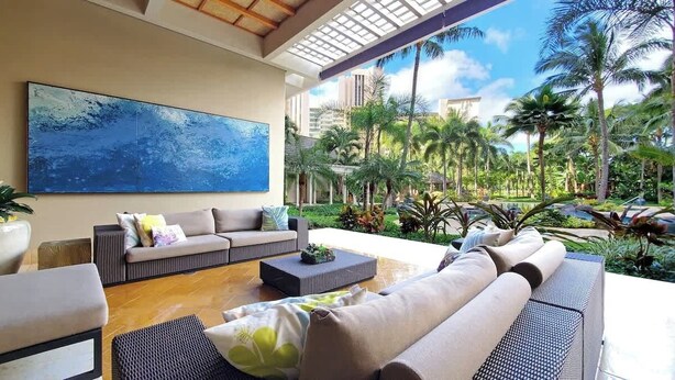 A spacious outdoor seating area with a sofa, chairs, and a coffee table. A large abstract painting is visible on the wall. - Marbella Lane- Prime Watermark Ocean & City View (Honolulu)