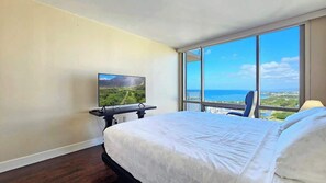A hotel room with a large bed, a TV on a stand, a chair, and a view of the ocean through large windows. - Marbella Lane- Prime Watermark Ocean & City View (Honolulu)